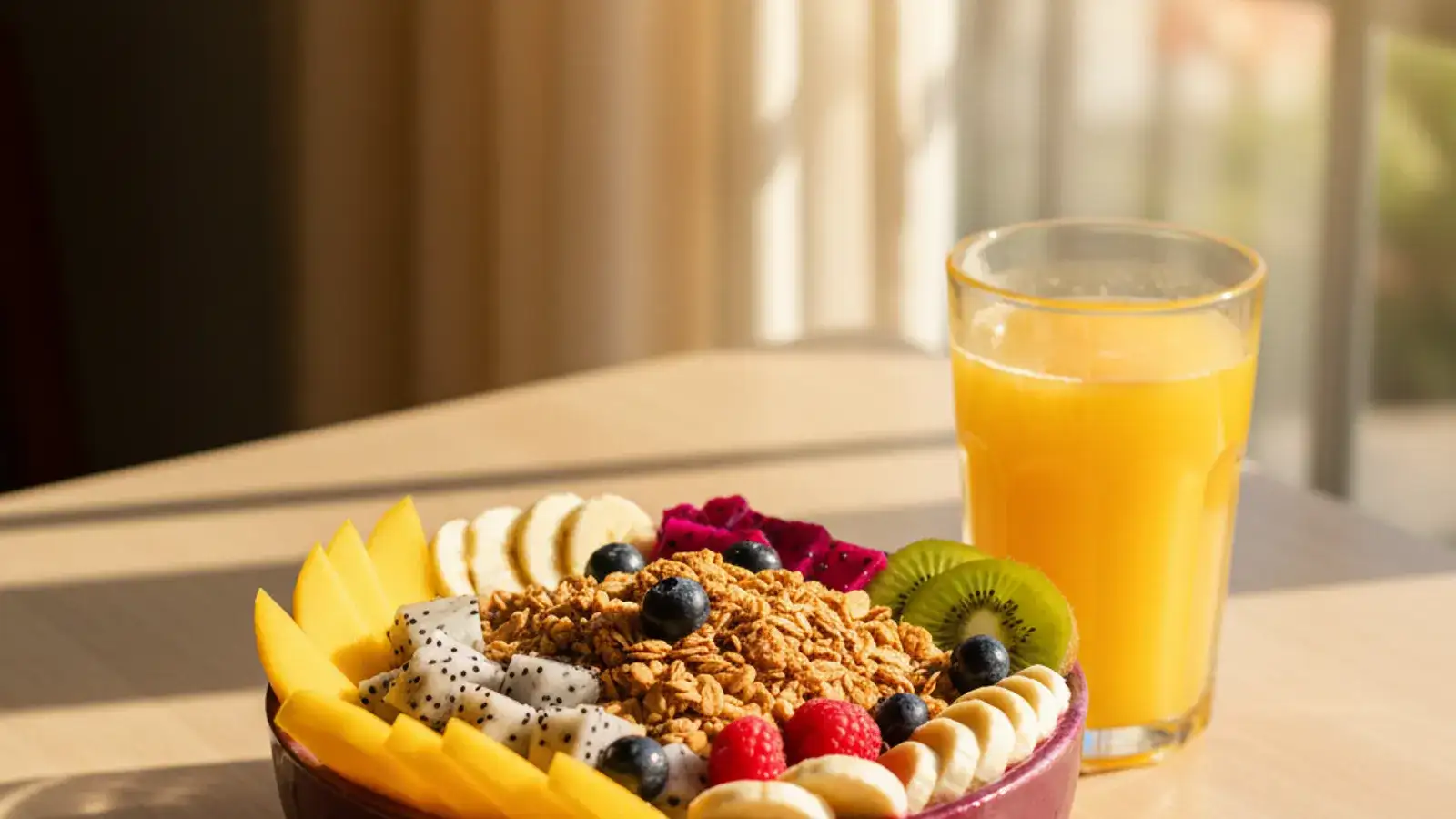 A bright pink dragonfruit smoothie bowl topped with granola, banana slices and coconut flakes on a wooden cafe table, with tropical greenery behind it.