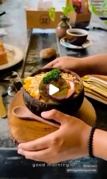 Mani che reggono una coppa di frutta frullata in un guscio di cocco, con mango, frutto della passione e scaglie di cocco