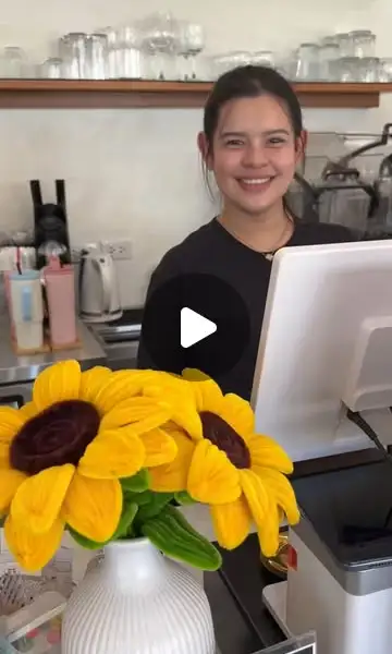 Barista sorridente dietro il bancone con un bouquet di girasoli davanti