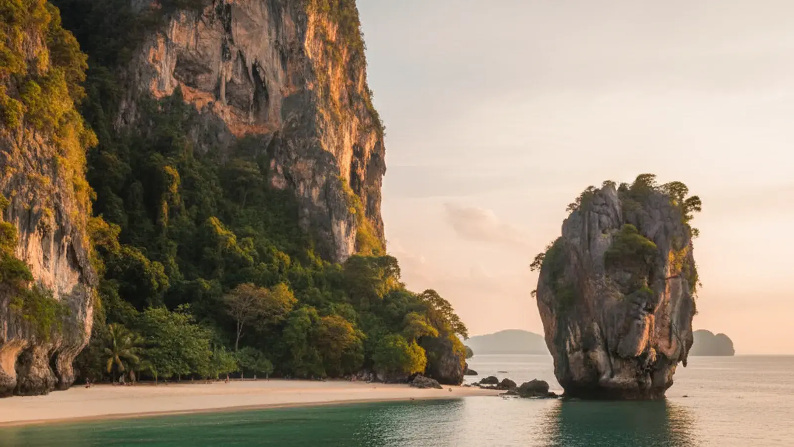 Longtail boat anchored in shallow turquoise water off Railay West beach, beneath a towering limestone cliff