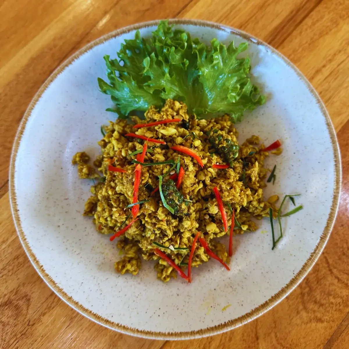 A spread of southern Thai dishes on a market table — a fiery dry chilli stir-fry, a bowl of sour orange curry, and golden turmeric fried fish