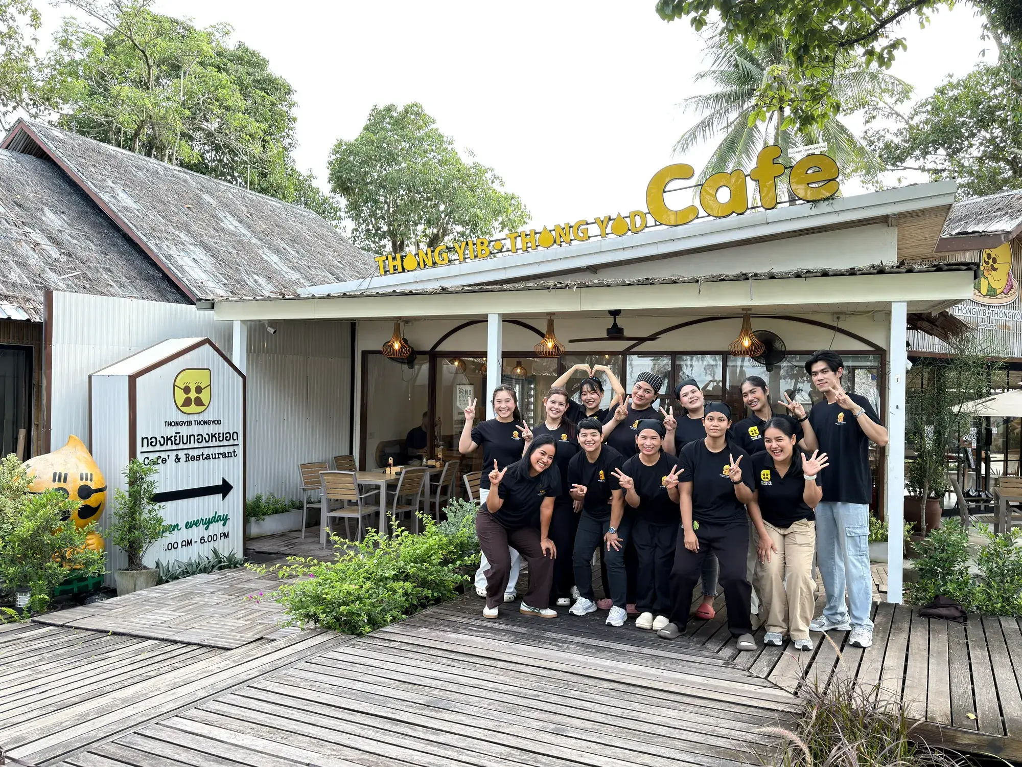 The full Thongyib Thongyod team cheering with arms raised in front of the cafe shopfront