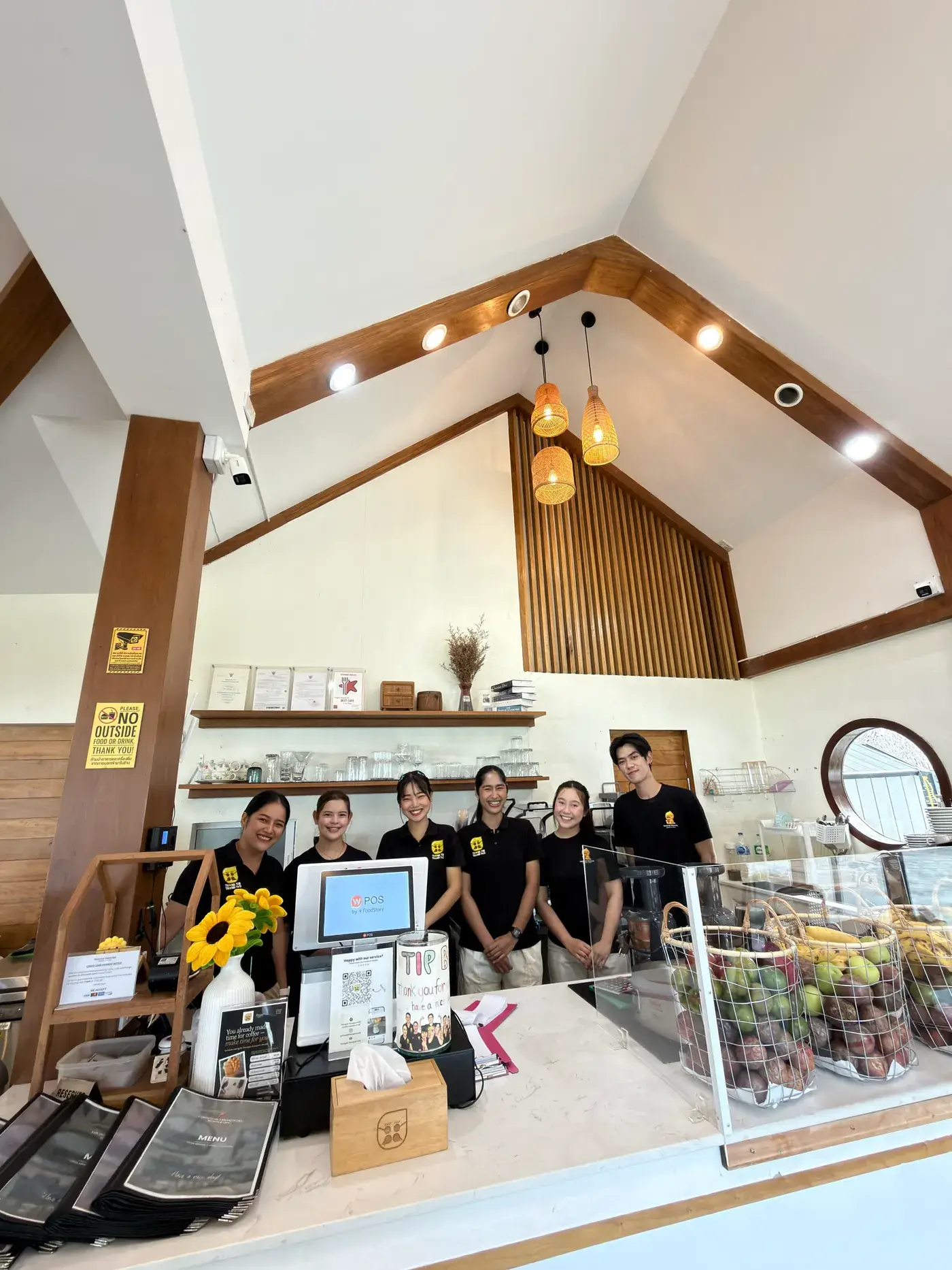 The team behind the counter under the wooden A-frame ceiling, sunflowers and fruit baskets in front