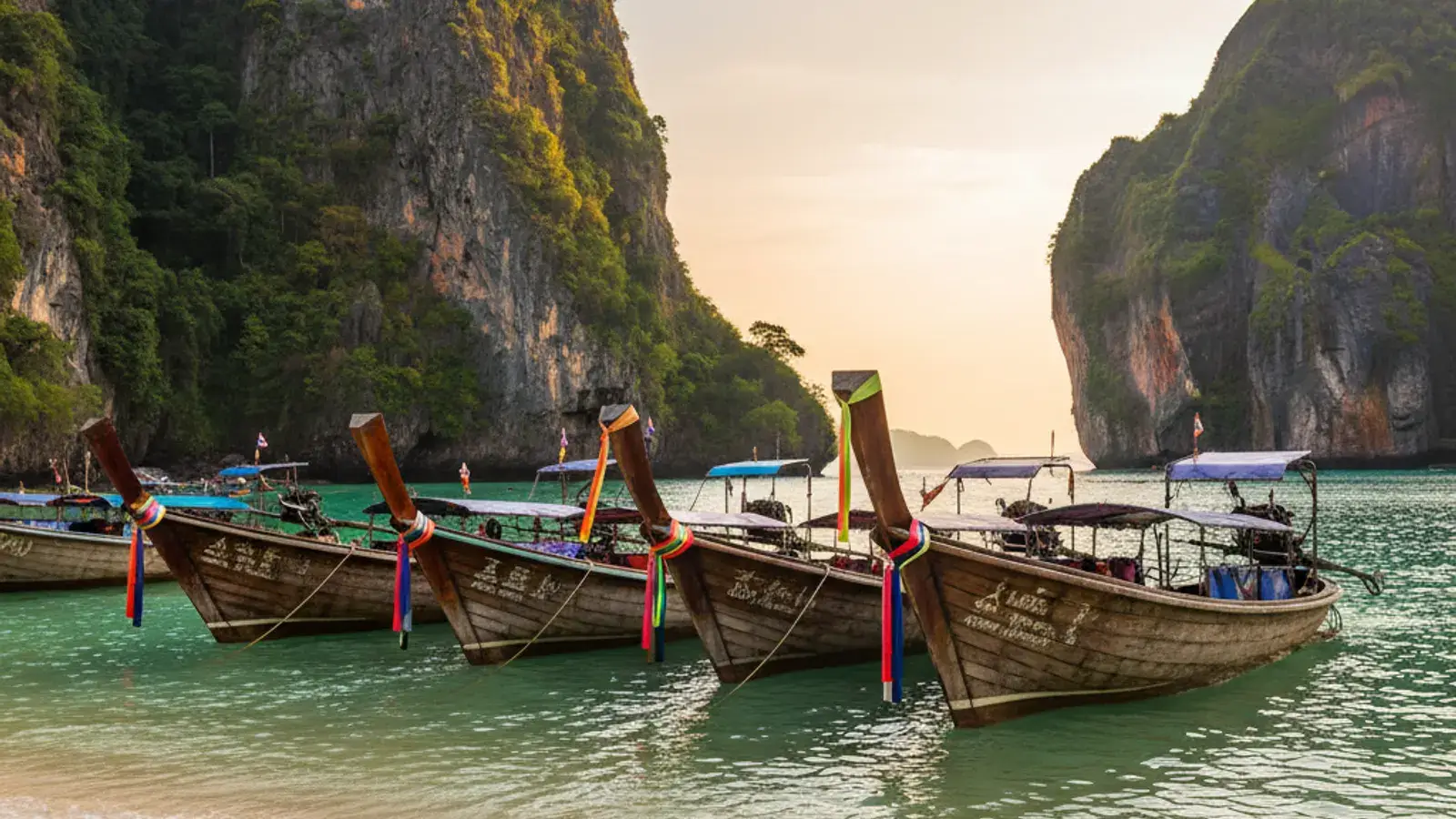 Longtail boats moored on Ao Nang Beach at golden hour, with limestone cliffs rising behind the bay