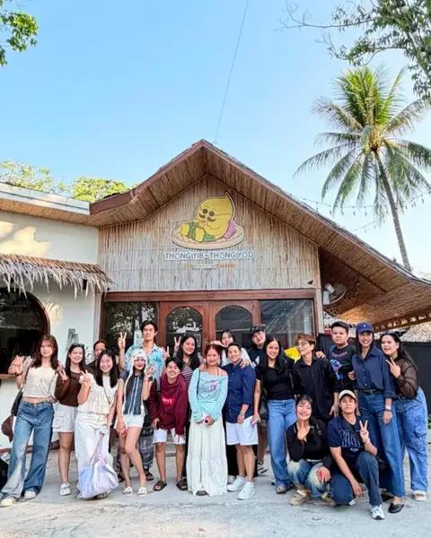 Tutto il team di Thongyib Thongyod posa davanti alla facciata in bambù sotto l'insegna della mascotte
