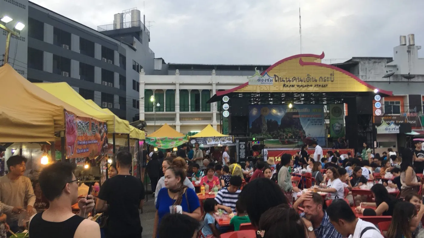 Crowds at red communal tables under the Krabi Walking Street archway, food stalls and a live-music stage behind them