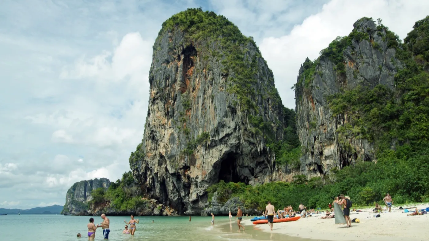 Phra Nang Cave Beach backed by a towering limestone cliff, with people swimming in shallow turquoise water