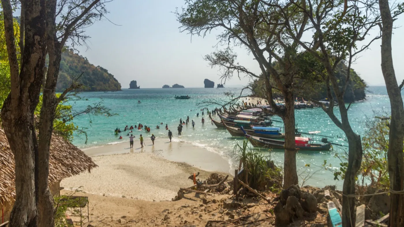 The white sandbar at Tup Island emerging from turquoise water at low tide, with longtail boats lined up along the shore