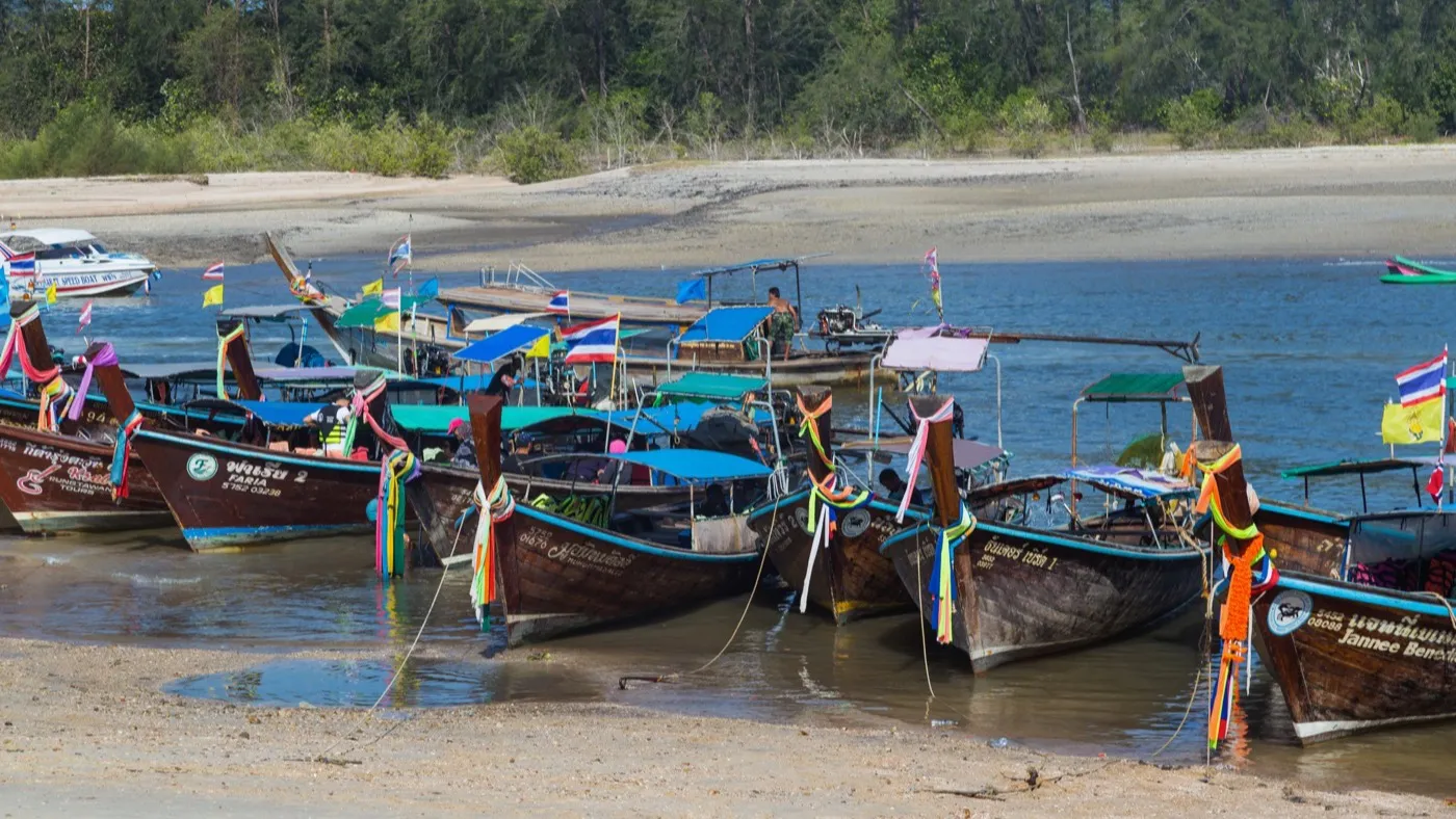 Brightly decorated longtail boats moored in the estuary channel by the Nopparat Thara pier, backed by mangroves