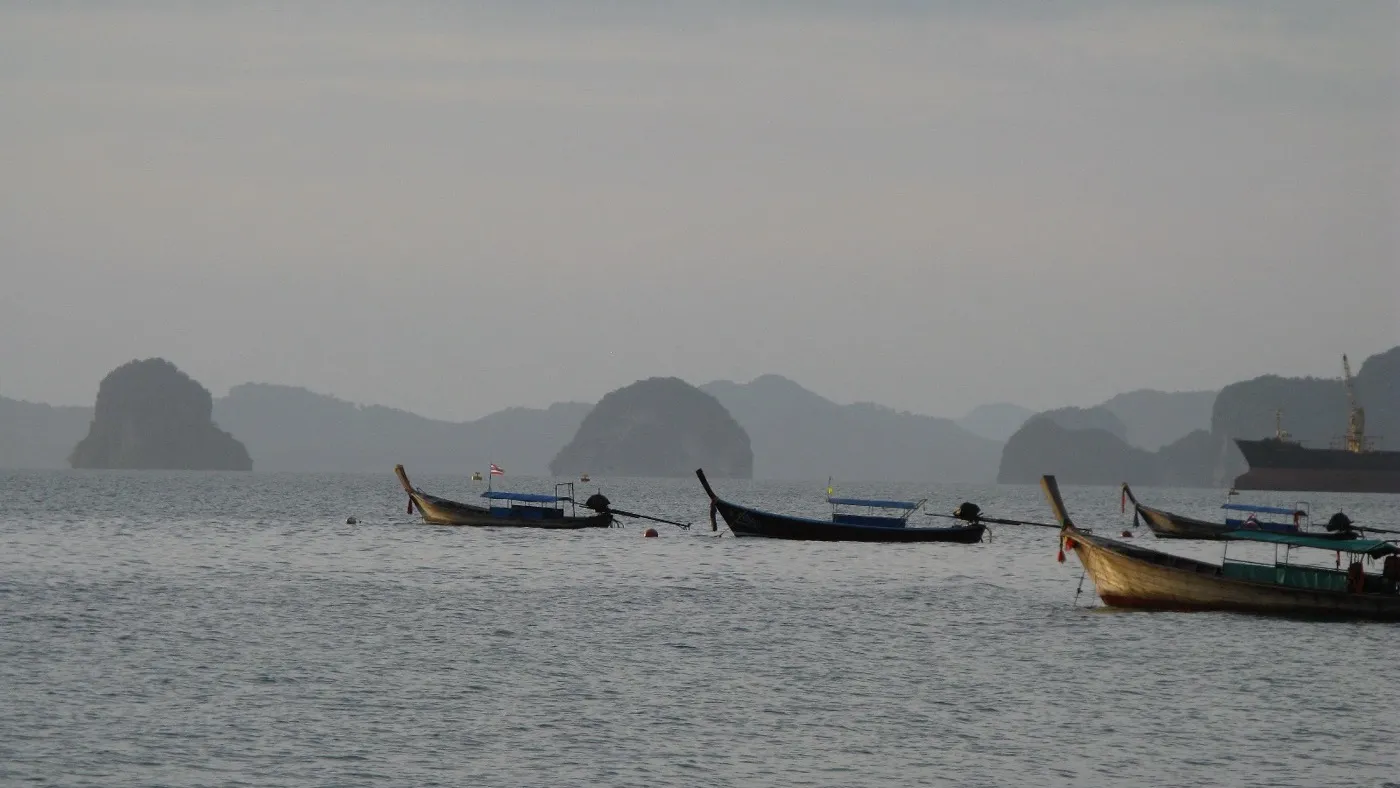 Longtailbåtar förtöjda på det lugna vattnet utanför Klong Muang Beach, med utspridda kalkstensöar över bukten