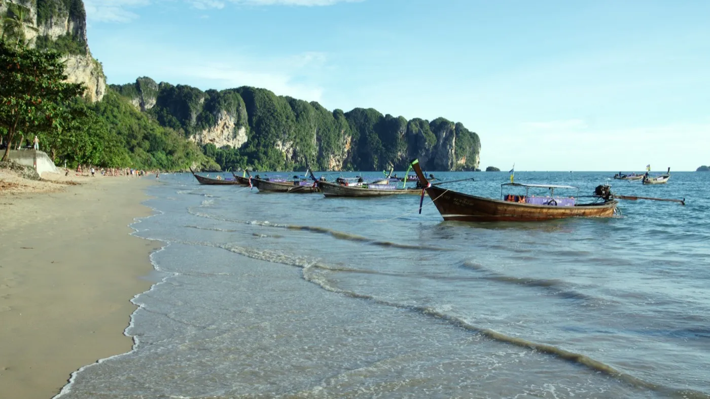 Longtail boats lined up on Ao Nang Beach with towering limestone karsts rising from the sea beyond